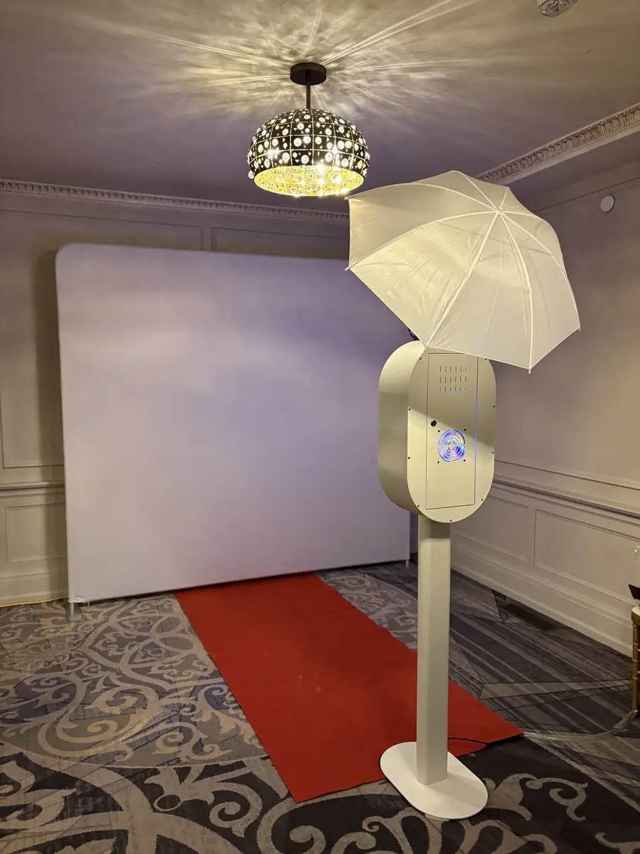 Modern white photo booth setup in a warm wedding venue.